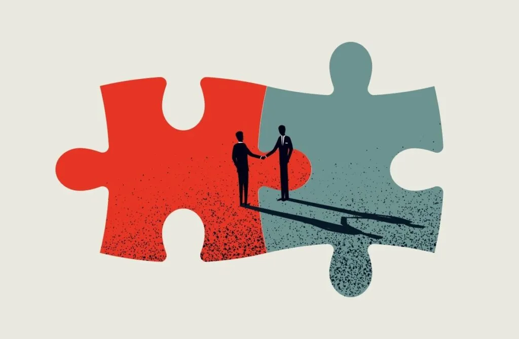 Image of two jigsaw pieces joined together - one red and one grey. In the middle of the pieces is a silhouette of two people shaking hands.